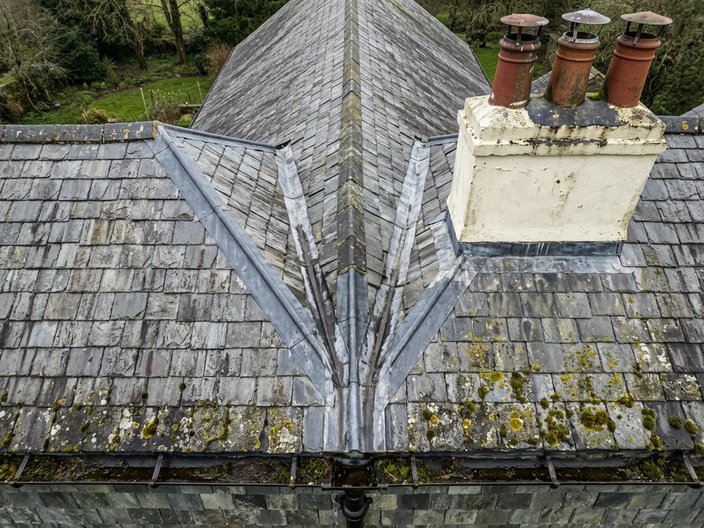 A close aerial view of a Devon slate roof showing the ridge, a lead valley and a rendered chimney stack with clay pots