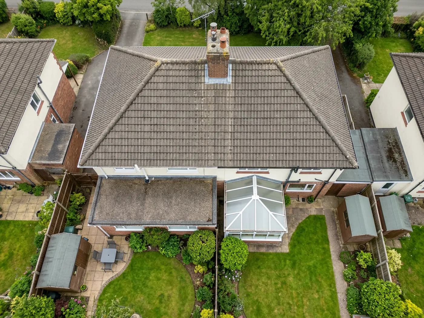 An aerial view down onto the roof and rear extension of a Devon semi-detached house, showing tiles, a chimney stack and a flat felt roof